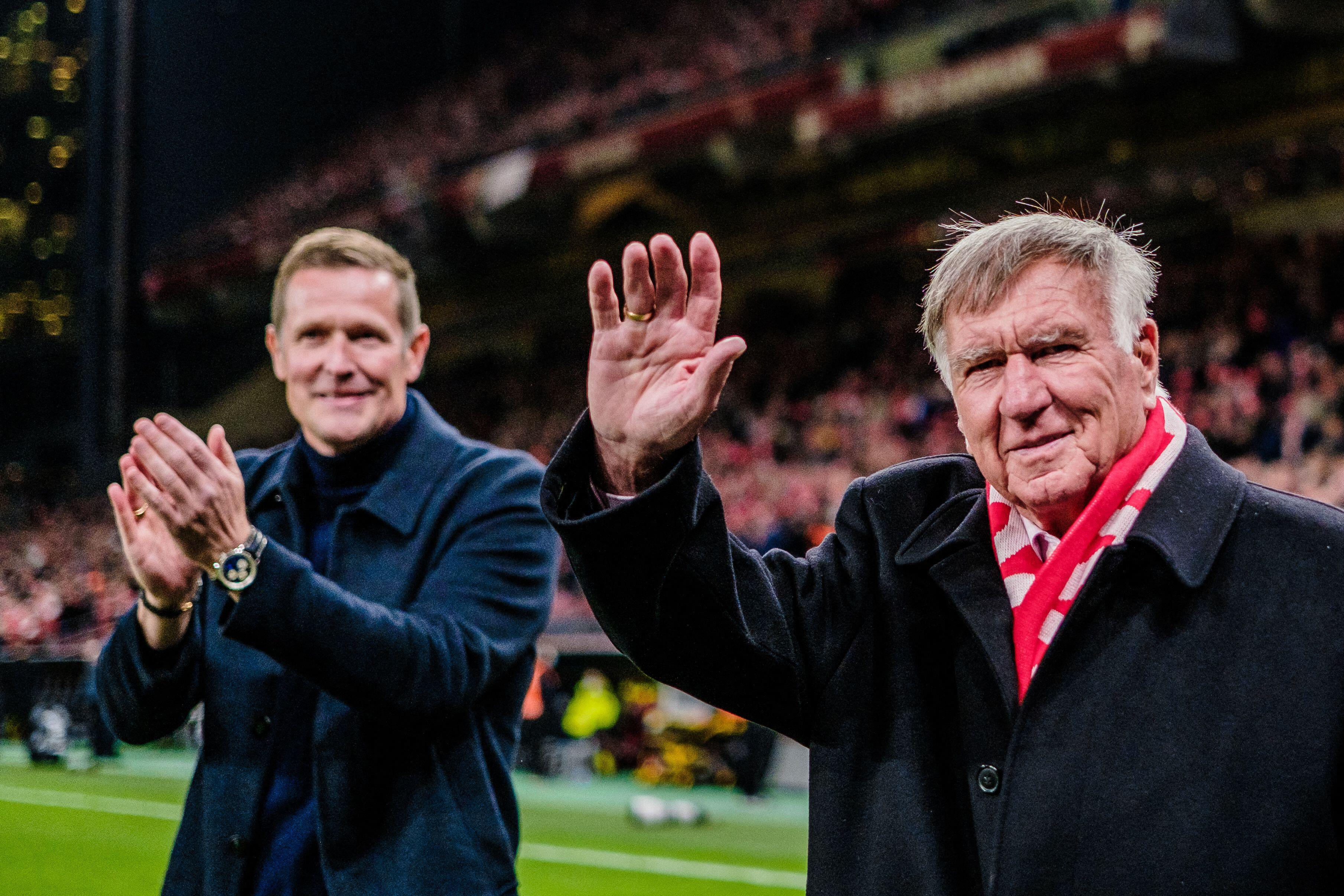 Former head coach Sepp Piontek waving to fans, while another man claps in the background.