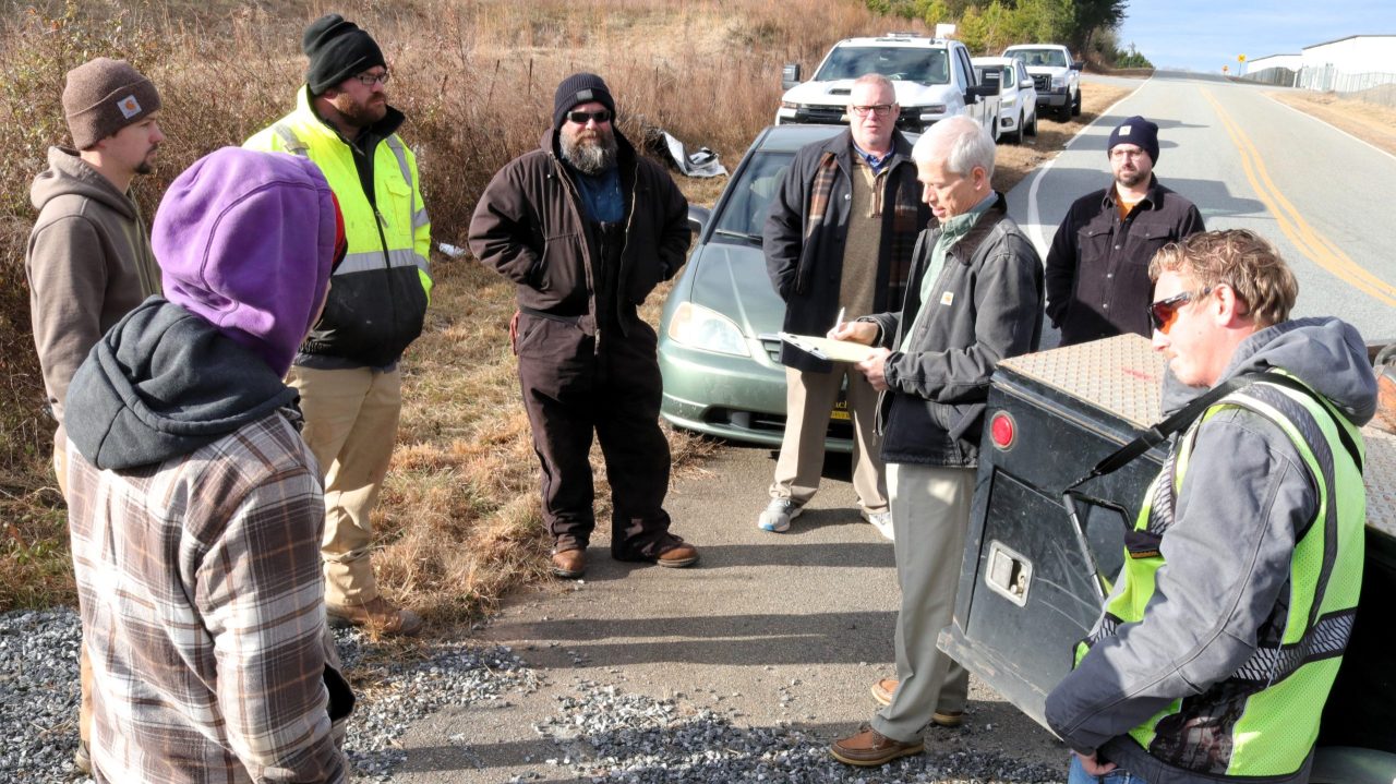 Men huddled around vehicles discussing the Alexander Industrial Park sewer project.