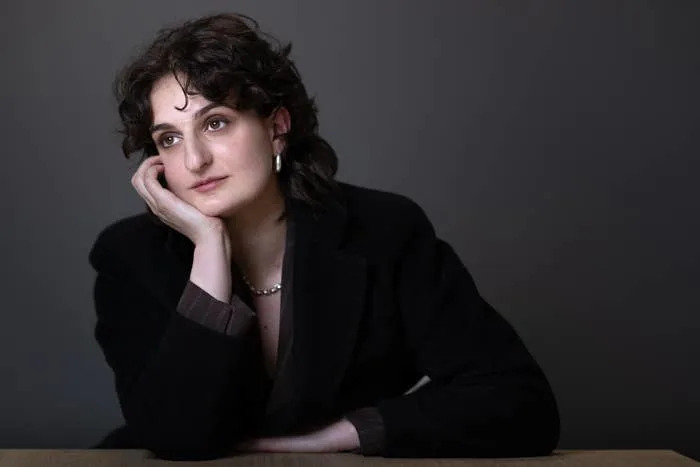 Person seated at a table, resting head on hand, in formal attire, looking thoughtfully into the distance