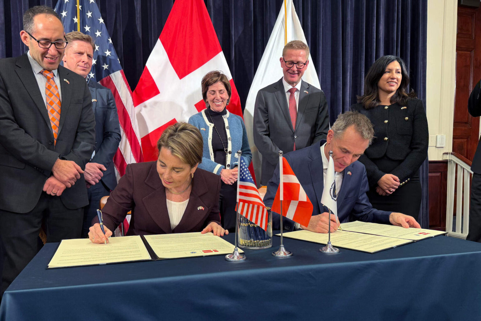 Gov. Maura Healey, left, signs a "collaboration agreement" with Danish ambassador Jesper Møller Sørensen, right, at the State House on Tuesday, Feb. 3, 2026. (Chris Van Buskirk/WBUR)