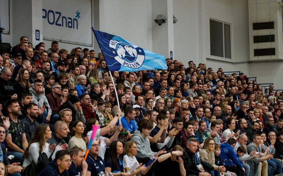 Supporters wave team flags and applaud during a basketball game.