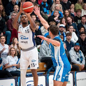 A player takes a jump shot over a defender during a basketball game.