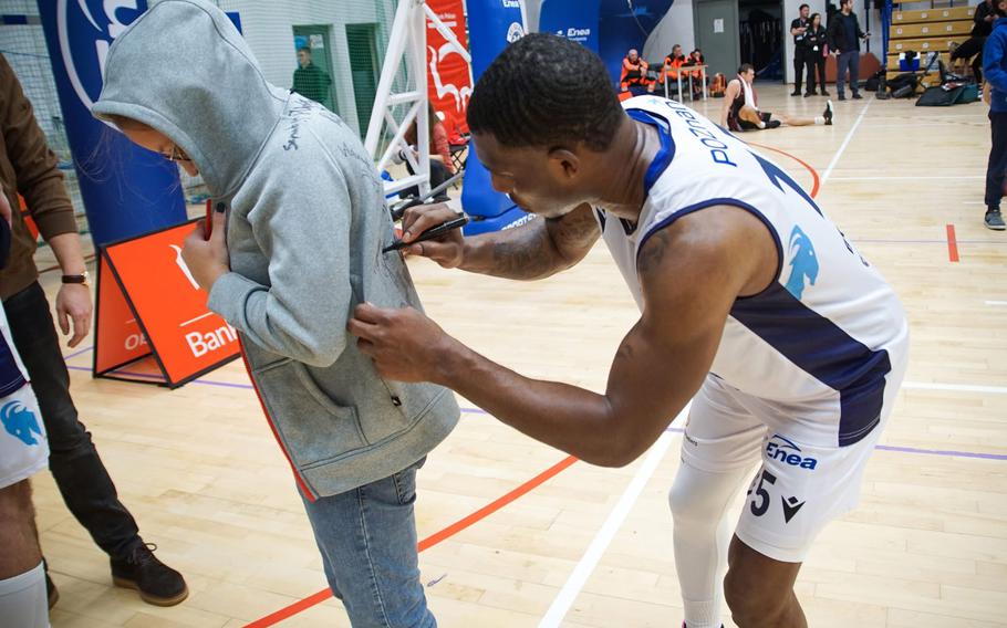 A basketball player signs an autograph for a young fan on the court.