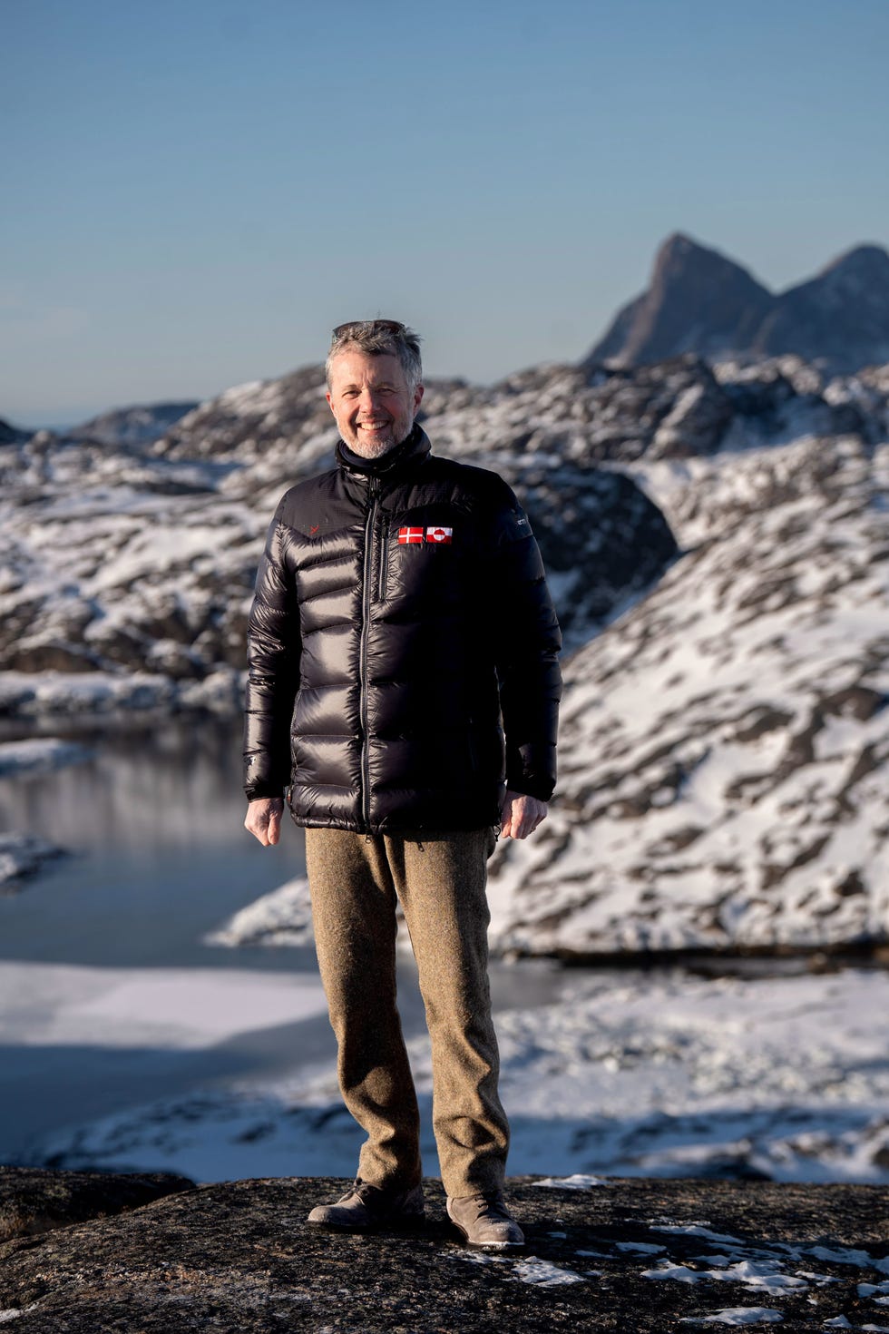 Person standing on rocky terrain with snow and water in the background