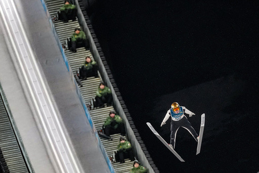 Italian Army soldiers on the steps of the ramp watch Domen Prevc, of Slovenia, soaring through the air during his first round jump of the ski jumping men