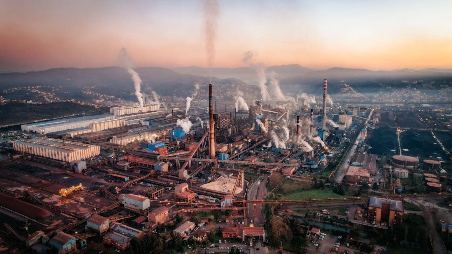 Air pollution joins Europe’s list of cancer risks Aerial view of a factory with chimneys emitting smoke during sunset, highlighting industrial pollution.