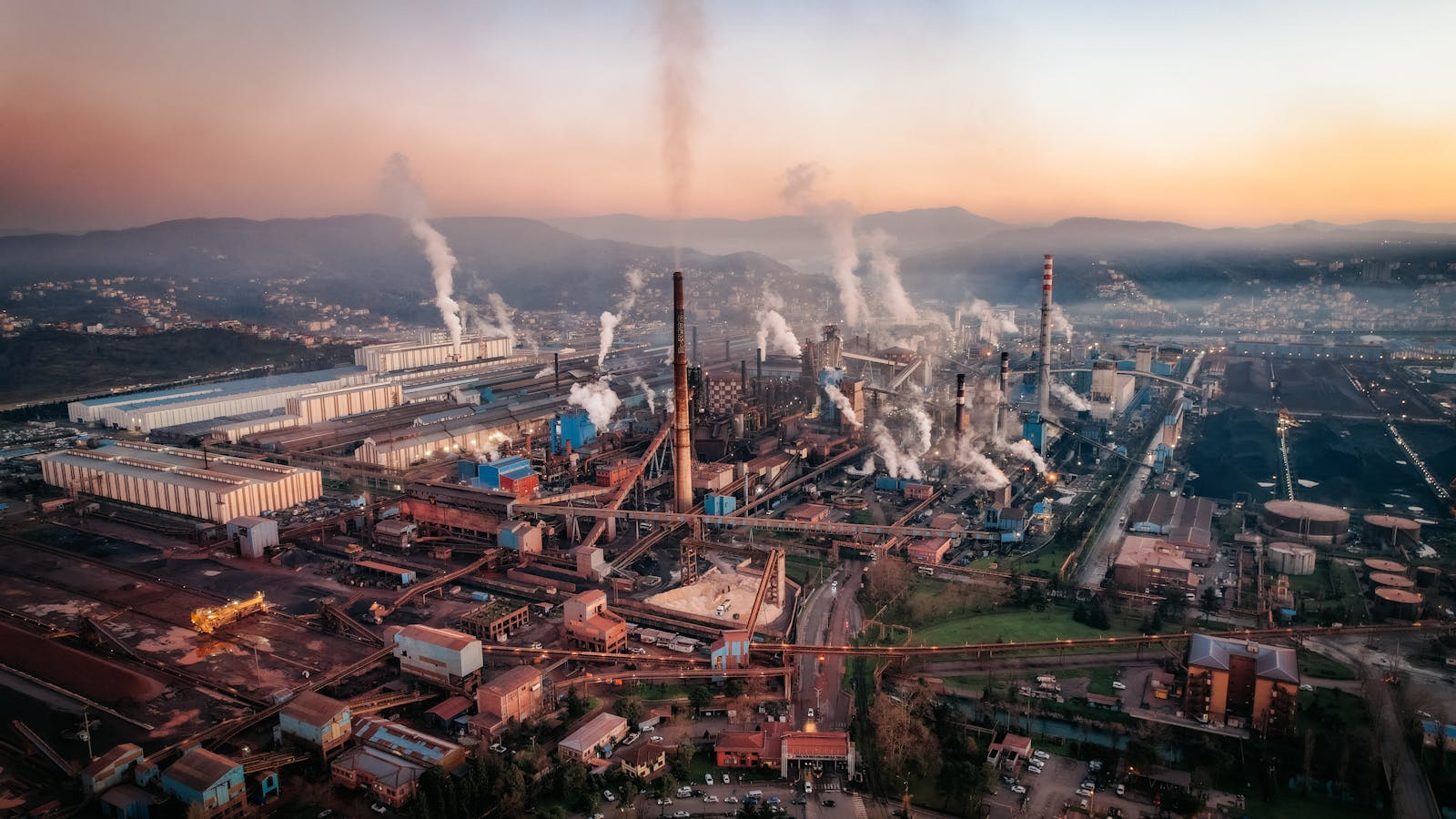 Aerial view of a factory with chimneys emitting smoke during sunset, highlighting industrial pollution.