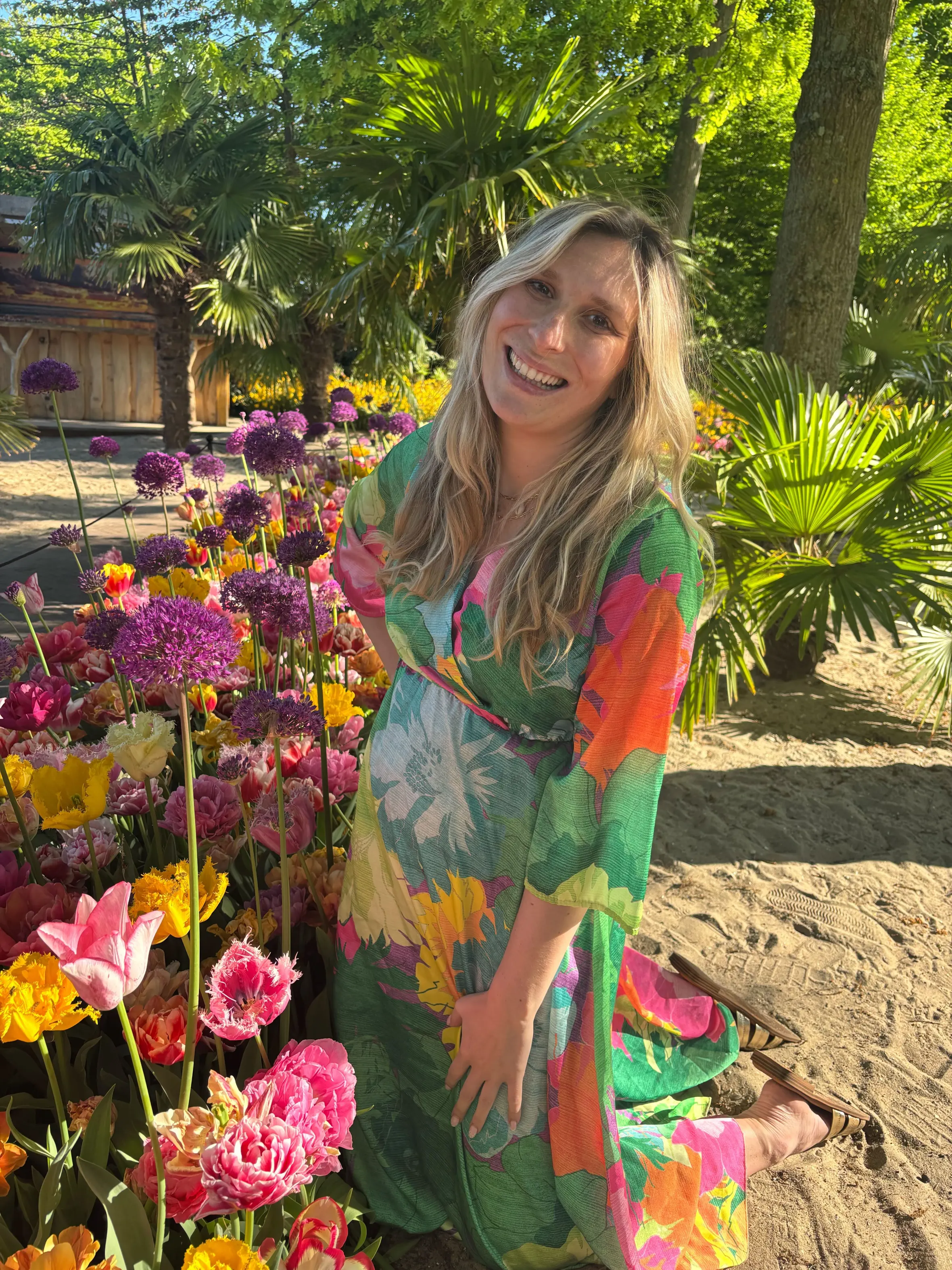 Lucy Holland kneeling in a garden of tulips, smiling at the camera.