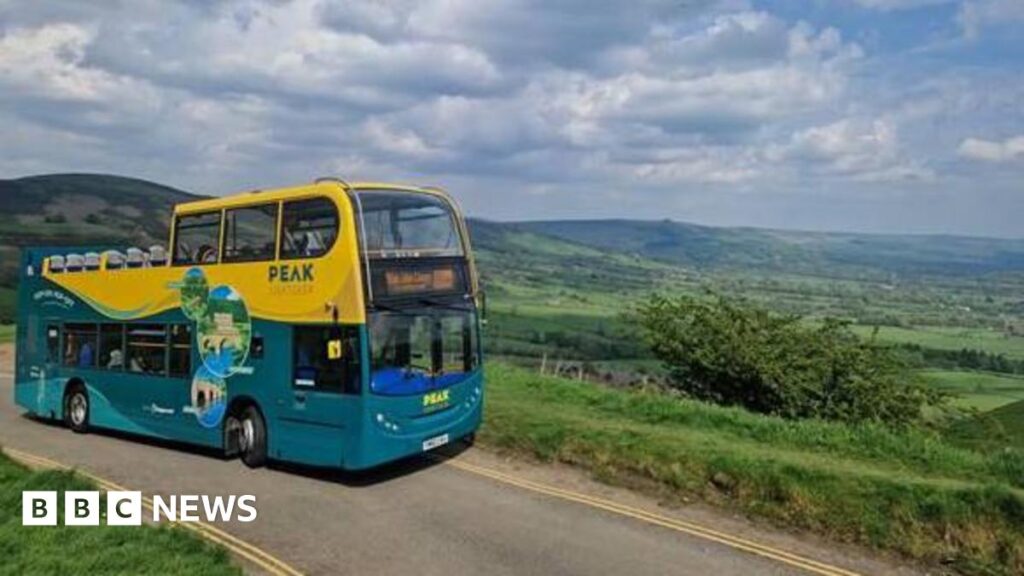 A open top yellow and green bus in the sunshine on a country lane with rolling green hills in the background.