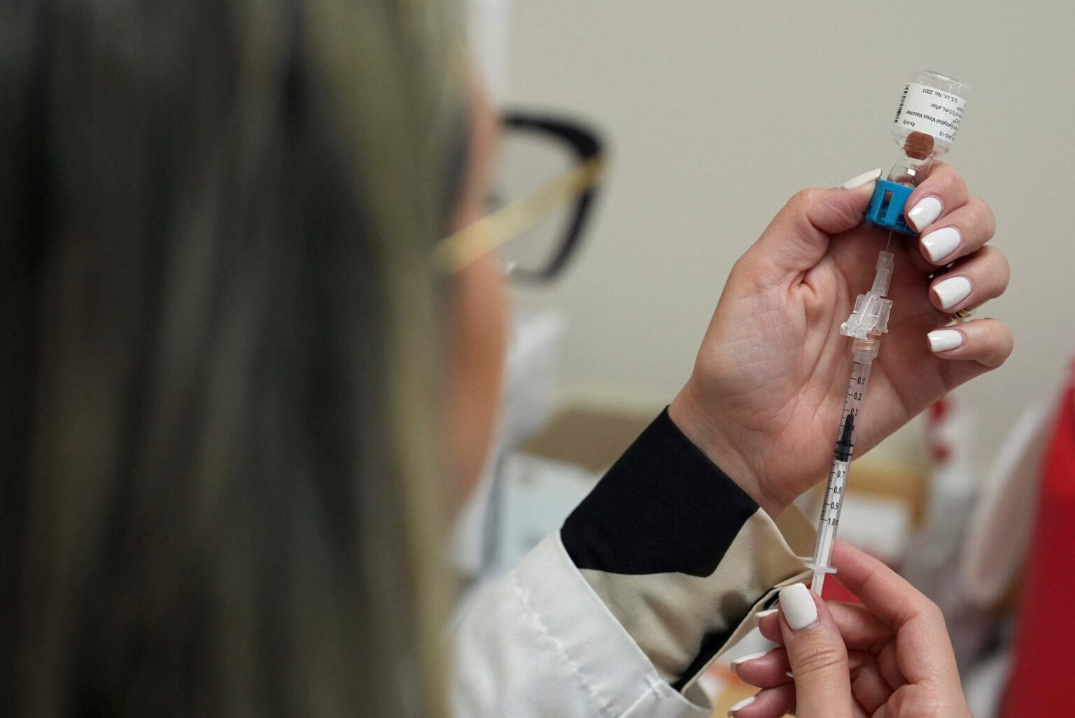 A person prepares a syringe with a vaccine, drawing liquid from a vial.