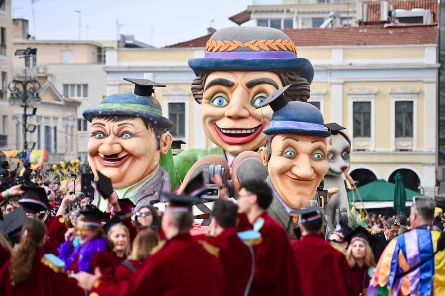 A vibrant crowd of carnival revelers marches through the central streets of Patras, dressed in colorful costumes, waving flags, and celebrating during the Grand Parade of the Patras Carnival.