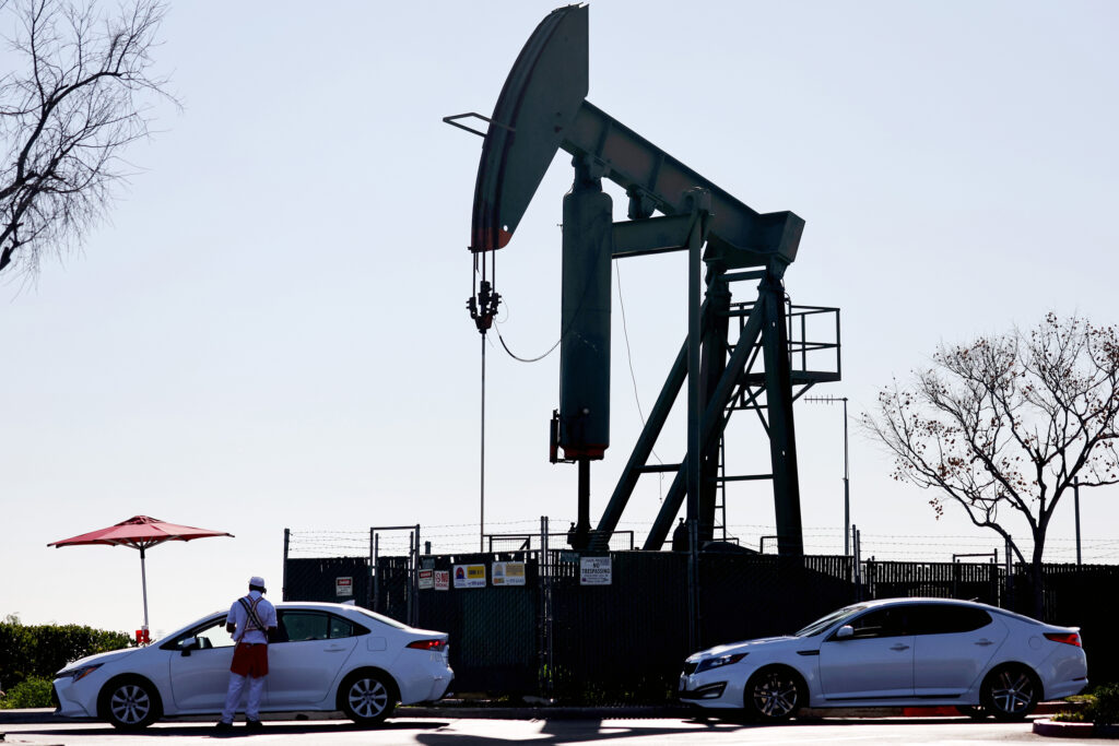 An oil pumpjack operates in the background as a fast food worker takes orders at a drive-through on Feb. 9, 2023, in Signal Hill, Calif. Credit: Mario Tama/Getty Images