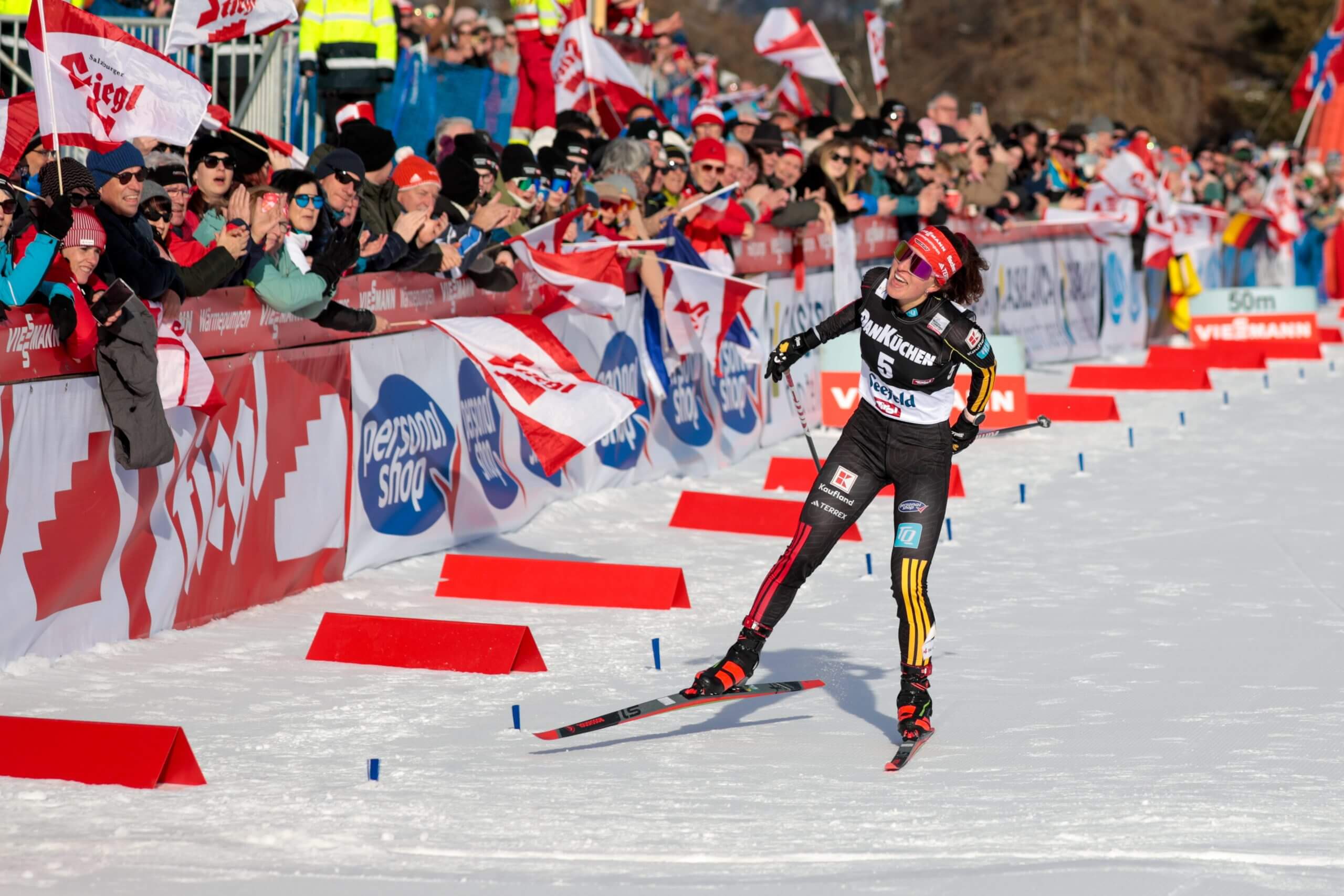 Nathalie Armbruster skies to the finish alongside fans waving flags.