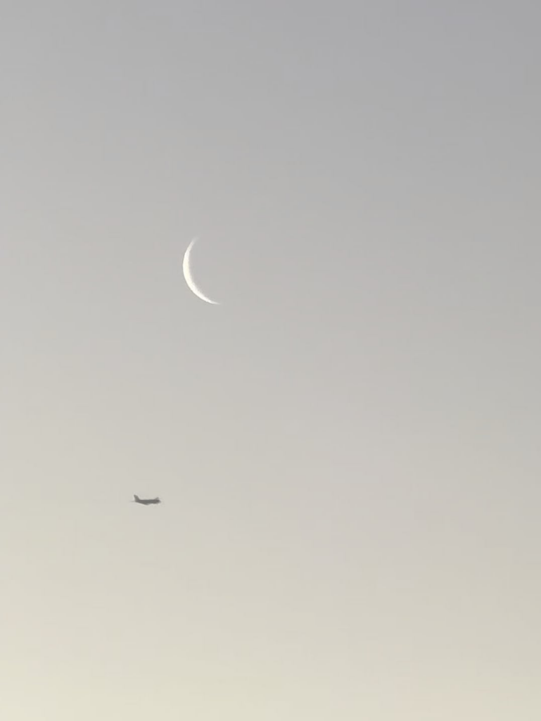 Aeroplane flying below a waxing crescent moon.