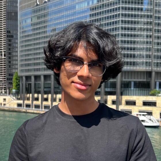 A young South Asian man with black hair and glasses, wearing a black T-shirt
