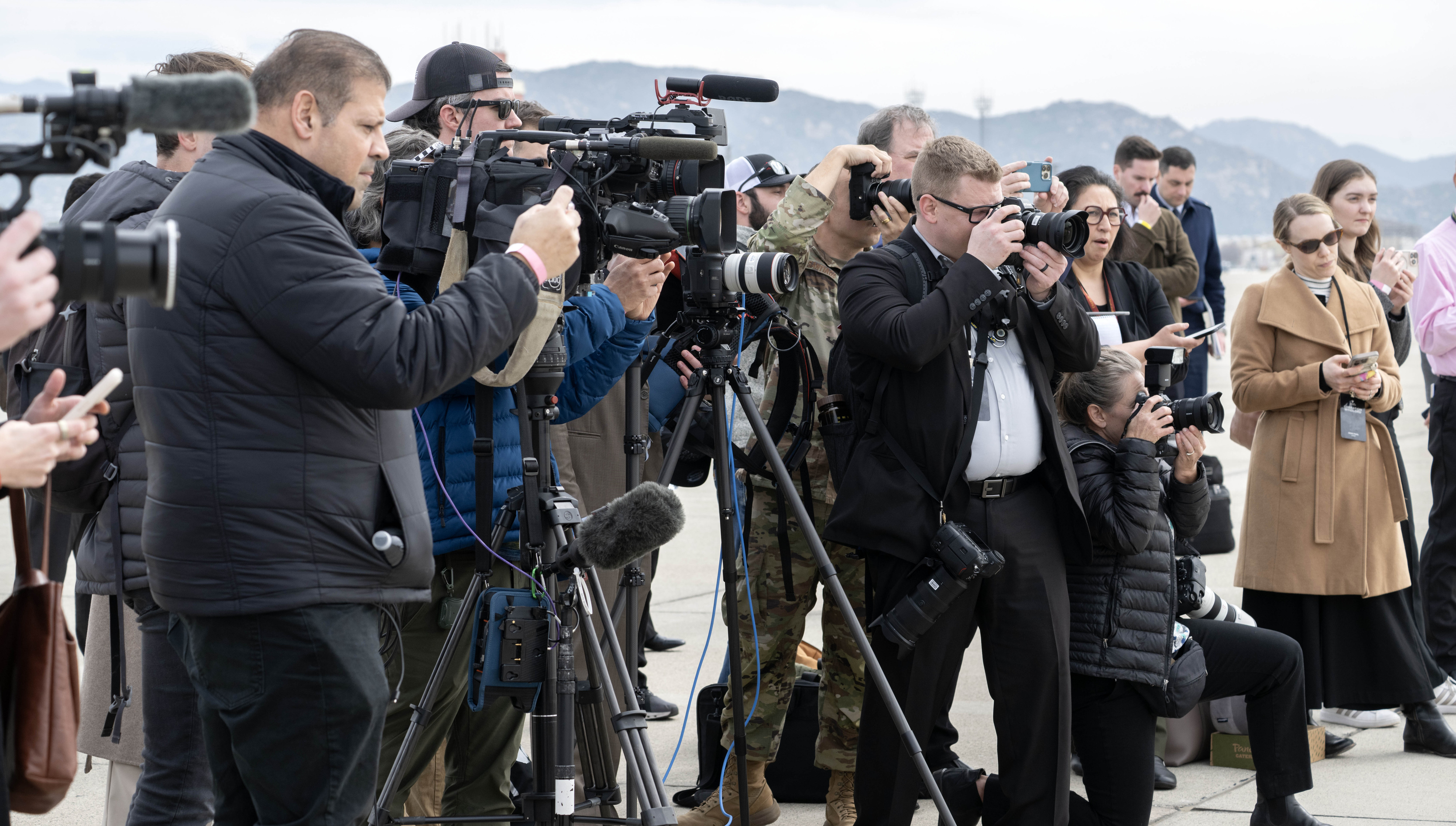 A gaggle of media gather on the tarmac of March...