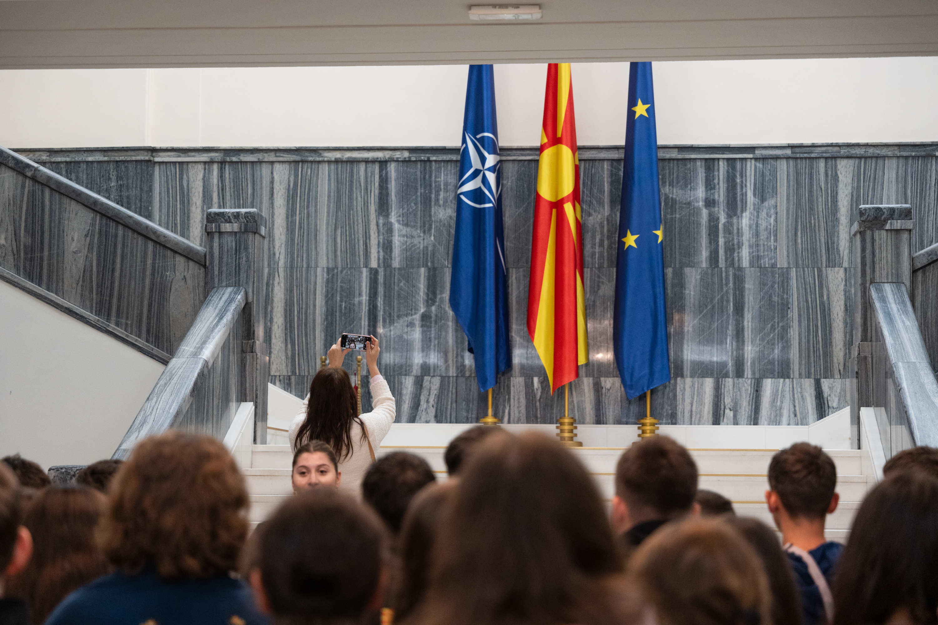 A person takes a selfie in front of a group, with the flags of NATO, North Macedonia and the EU in the background.