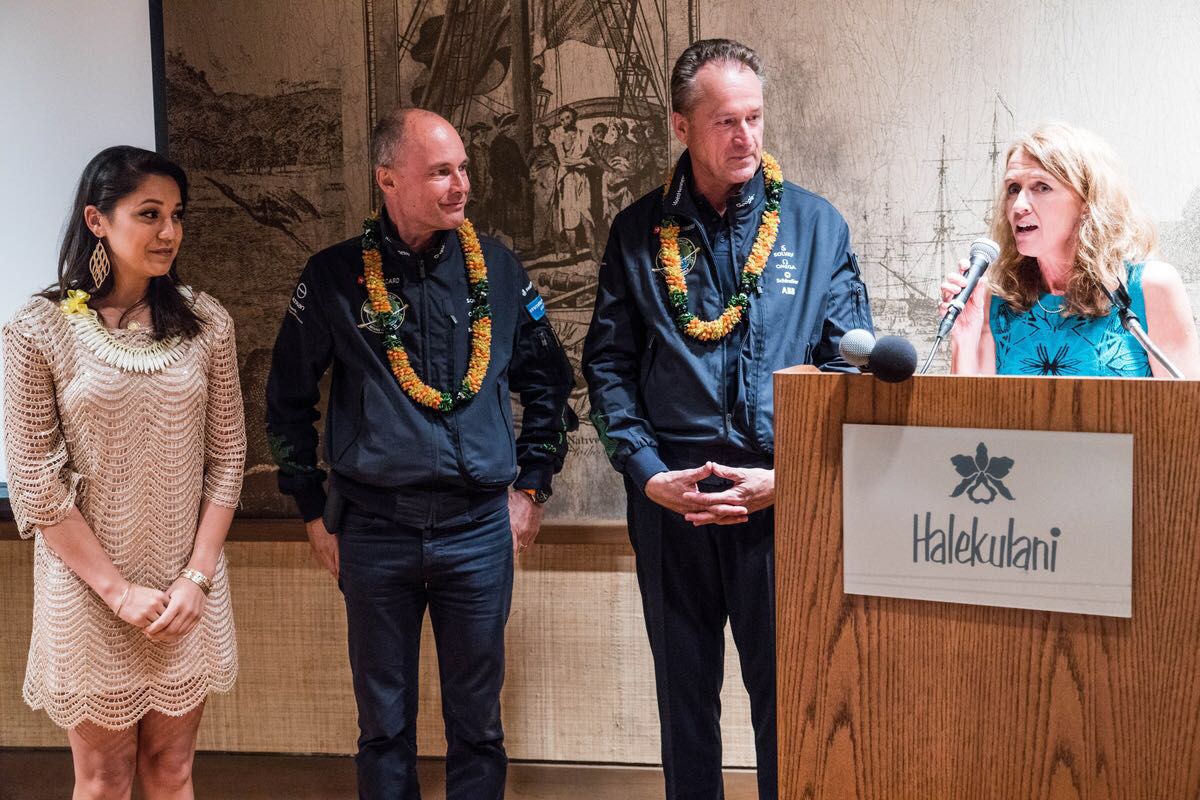 Two women and two men, both wearing flower garlands around their necks, one of the women is giving a speech.