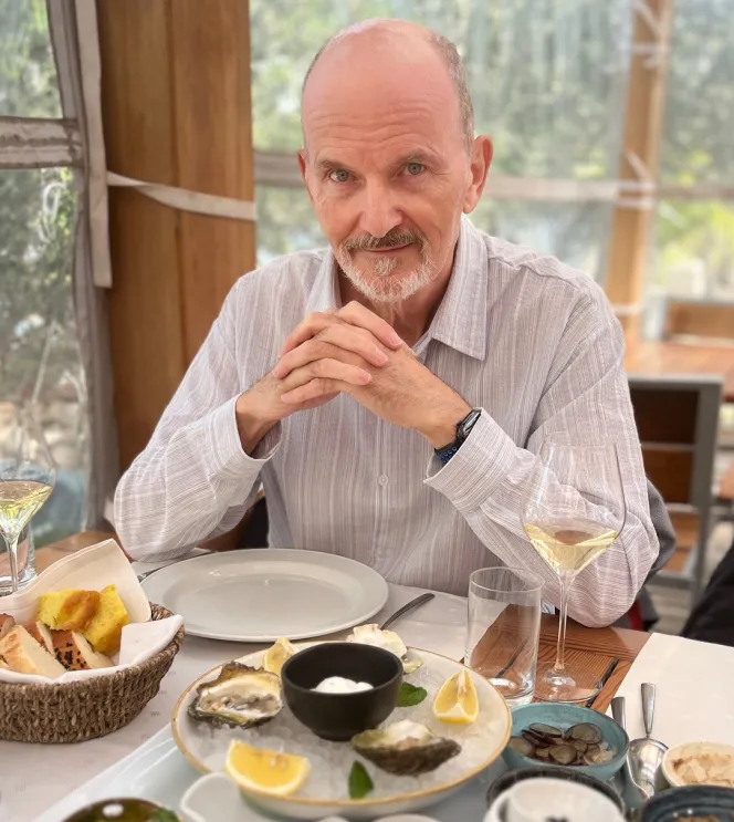 A man with a white beard sitting at a table with oysters and other dishes.