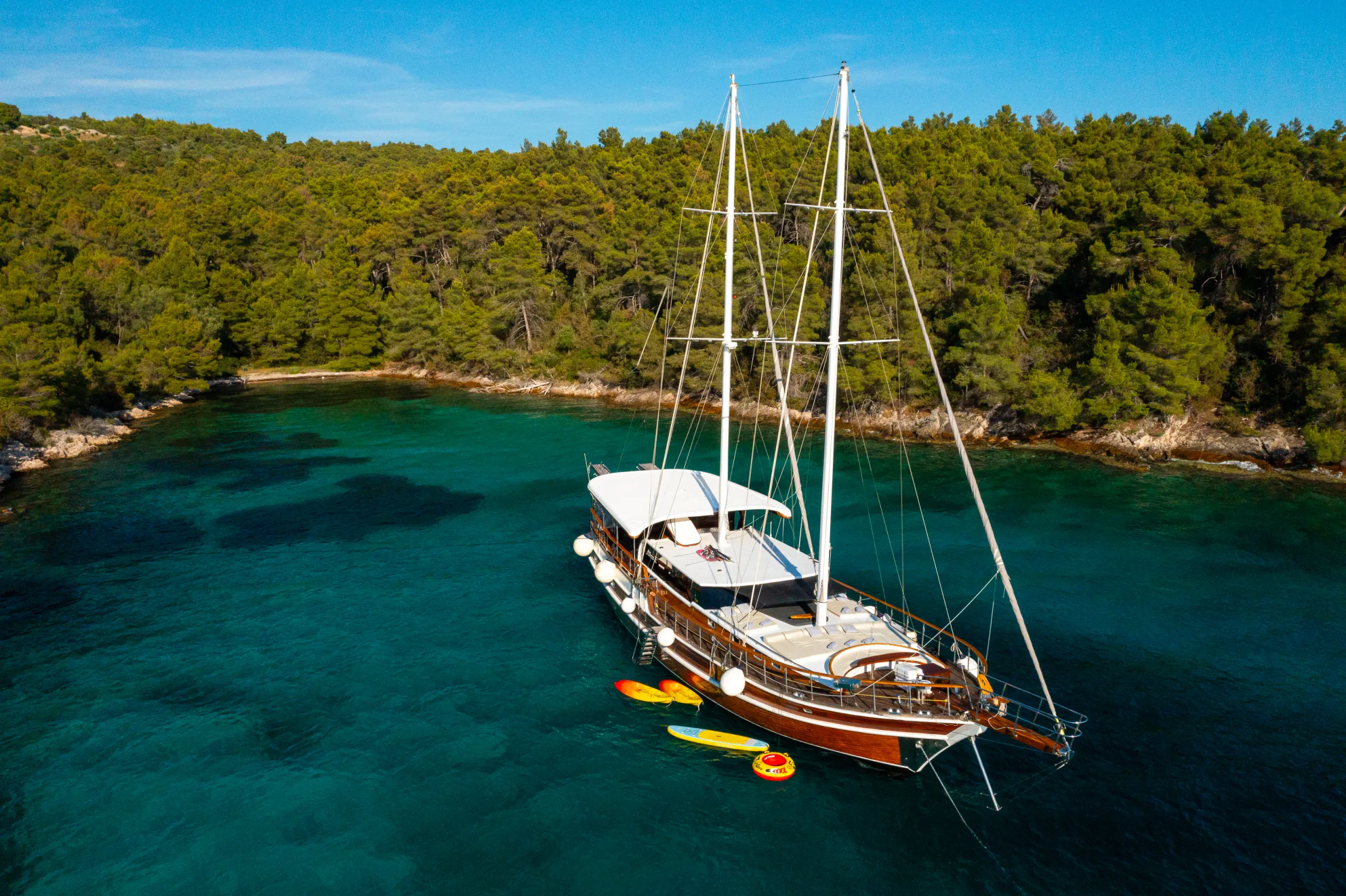 An aerial view of the Allure sailboat anchored in a bay, with a forested coastline in the background.