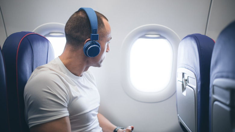 Man wearing blue headphones on an airplane window seat