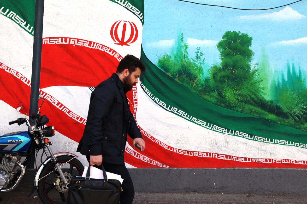 An Iranian man walks past a mural of an Iranian flag in Tehran, Iran on Feb. 22, 2026. (AFP Photo)