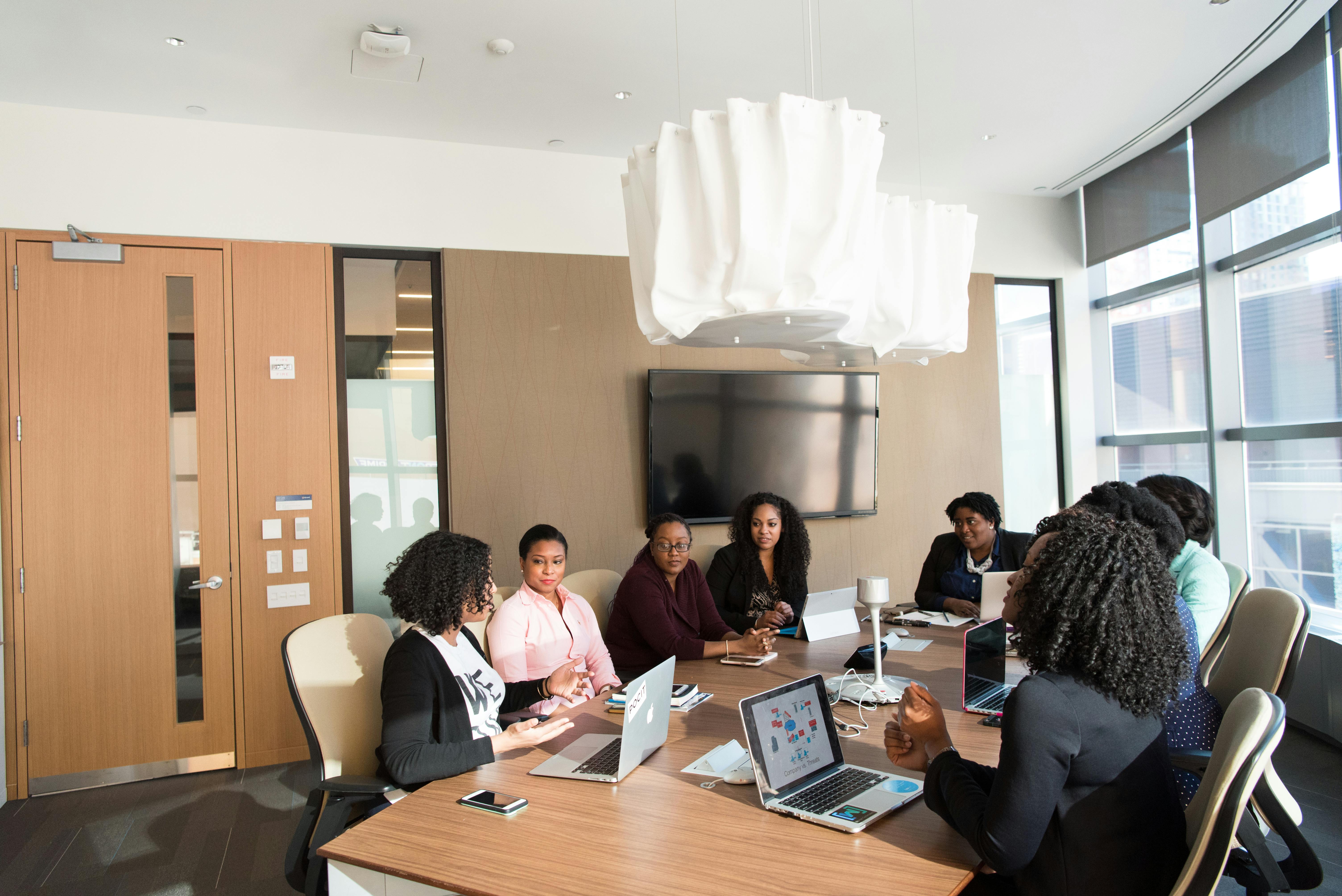 Group of women collaborating at a conference table with laptops in a modern office meeting room.