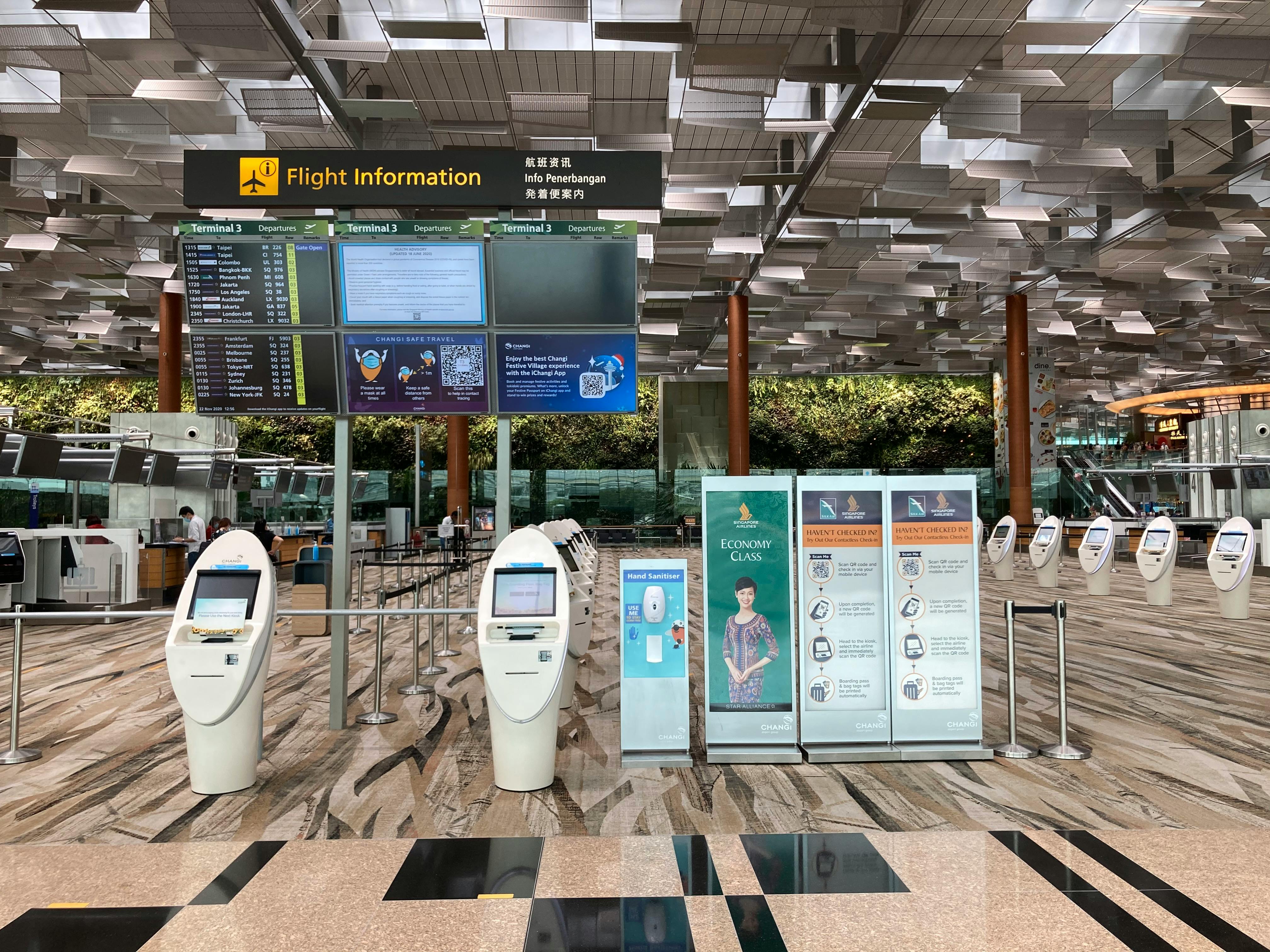 Self-service check-in kiosks beneath a flight information display in an airport departure hall.