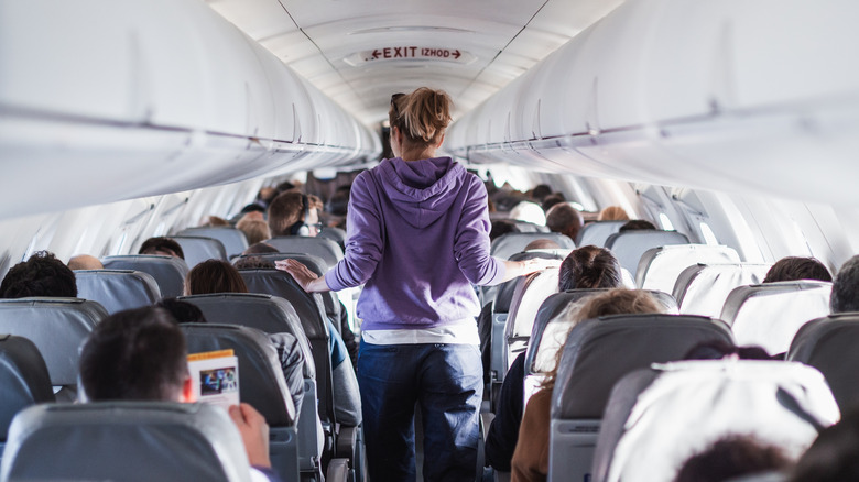 Woman in purple jacket walking down a plane aisle