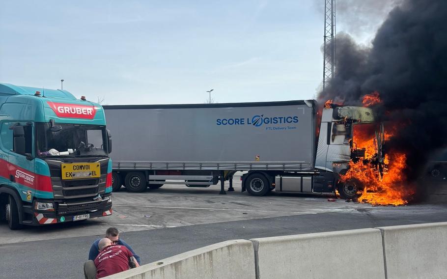 Brian Bailey helps a man on the road while a semi-truck is on fire in the background.
