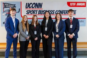 Group of UConn students gather in front of the UConn Sport Business Conference banner.