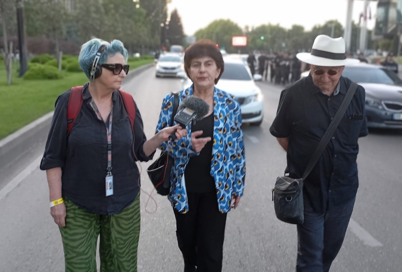 A woman with a microphone is talking to a woman in the middle while a man is on the other side listening... they are walking on the road during a march
