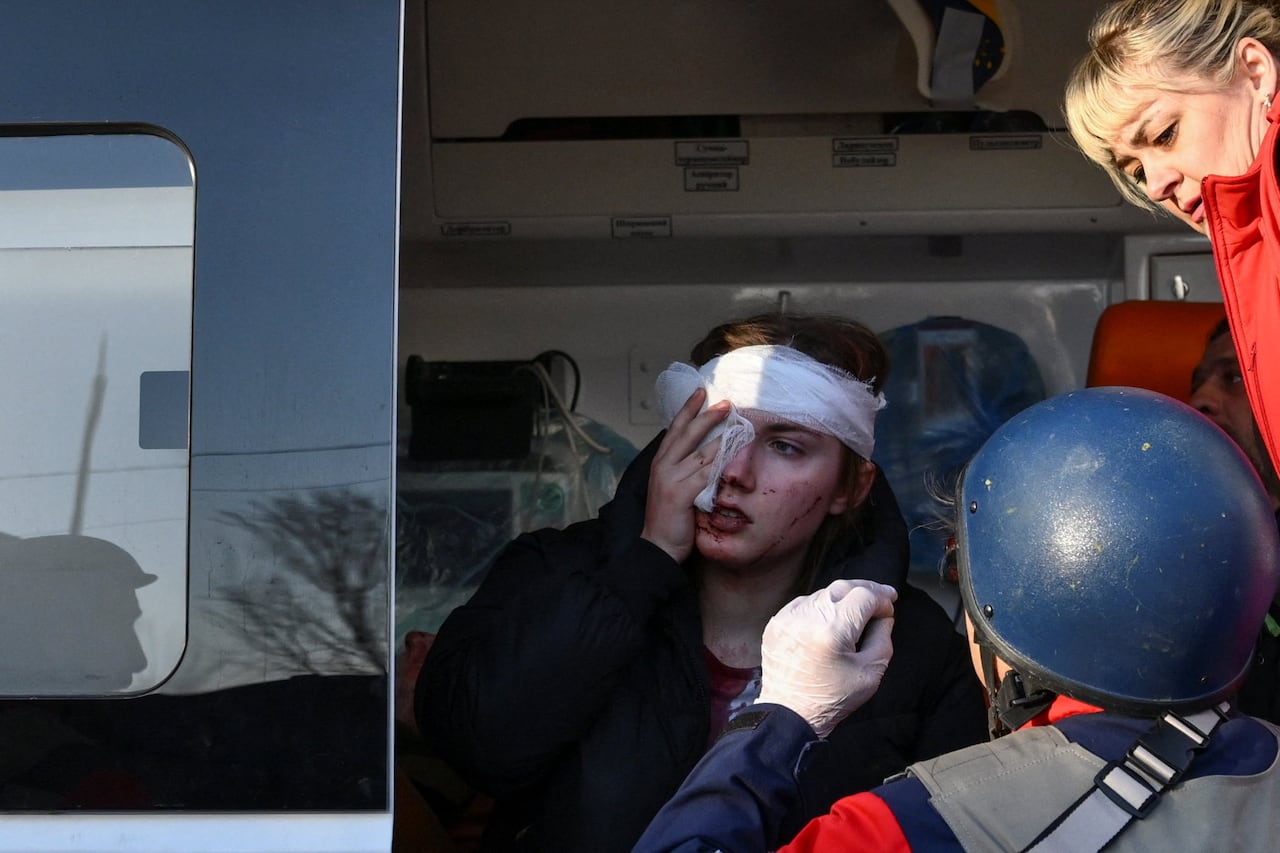Paramedics attend to a person holding gauze to their face.
