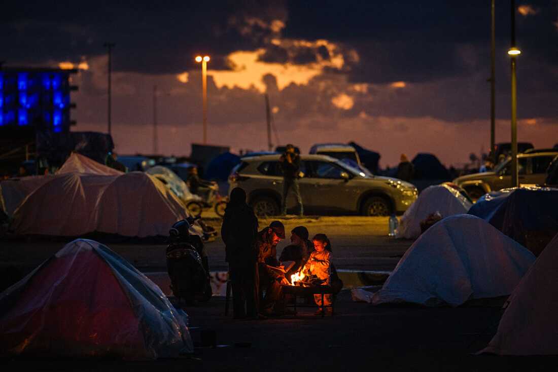 Displaced people warm up around a fire outside their tent along Beirut's seafront area on March 30, 2026.