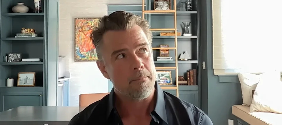 Man in a dark shirt in a thoughtfully furnished room with shelves and artwork in the background