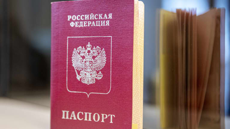 A red Russian passport with Cyrillic lettering standing on a shelf, with a mirror image of the document's open pages seen in the background.