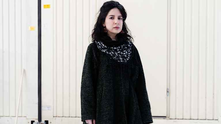 A dark haired woman stands outside.