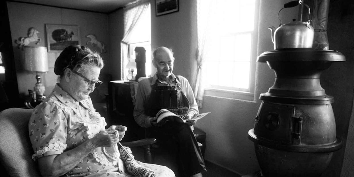 A farmer and his wife sit in front of their wood stove.
