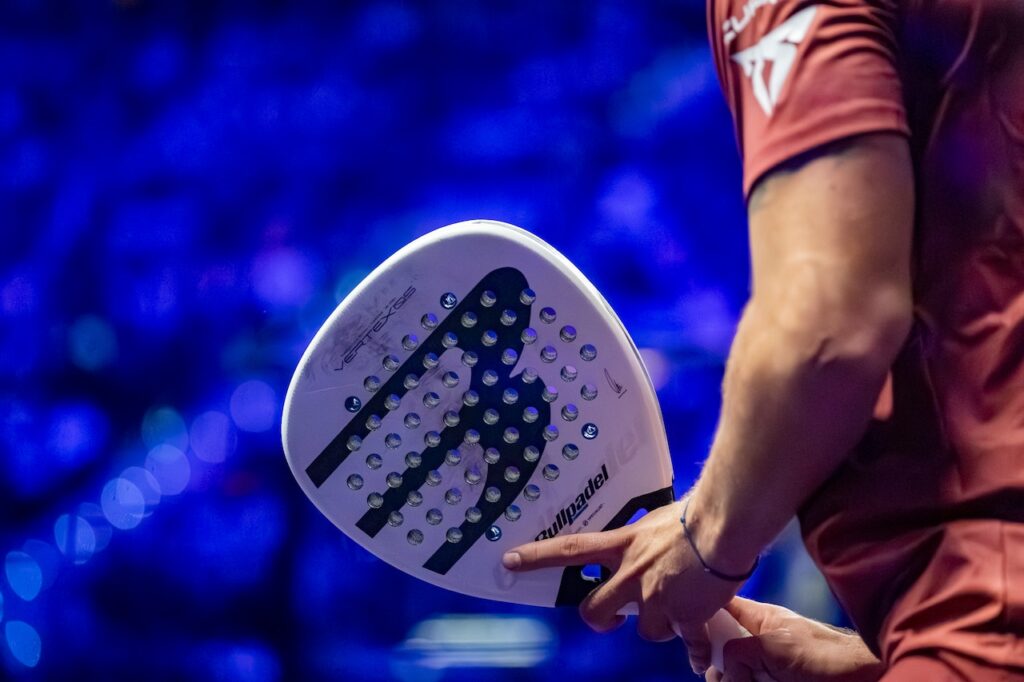 Close up of person in orange shirt holding a white padel racket