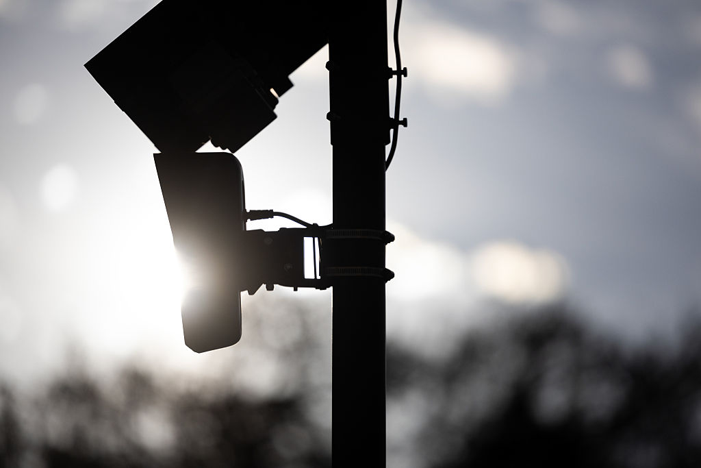 A silhouette of a Flock security camera mounted to a street pole.