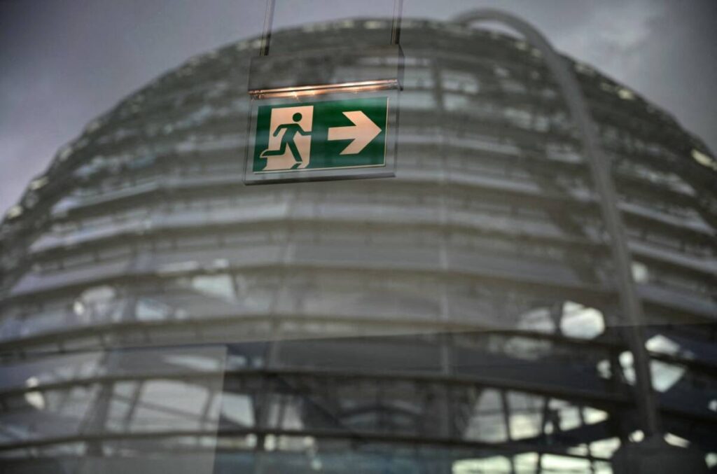The cupola of Germany’s Bundestag is seen behind a sign indicating the way to an emergency exit on the sidelines of a debate focusing on immigration, 31/1/2025 (Tobias Schwarz/AFP)