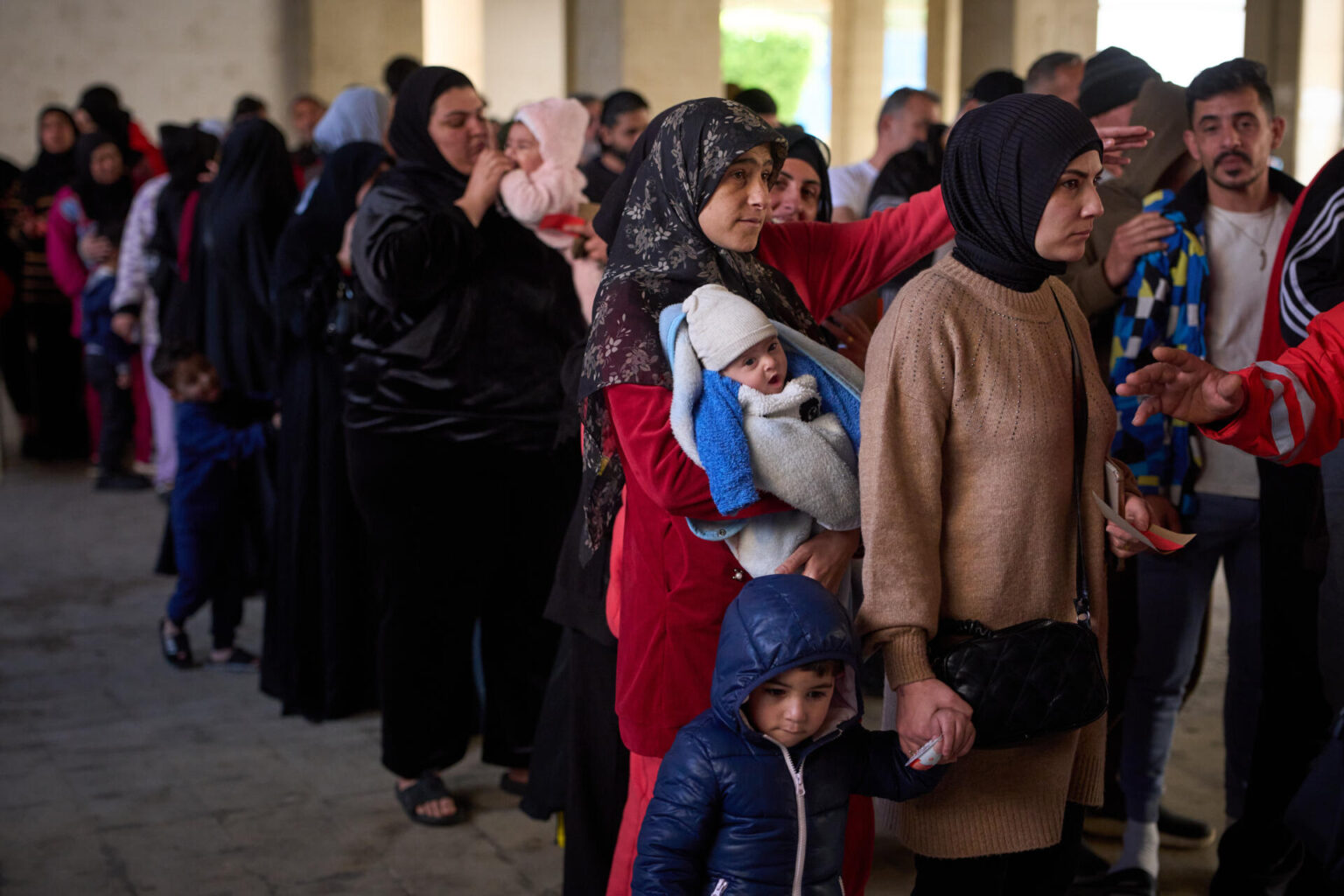 Displaced men and women with their children from Beirut's southern suburbs, wait to receive donated food rations inside a school converted into a shelter in Beirut, Lebanon, Friday, March 27, 2026. (Emilio Morenatti/AP)