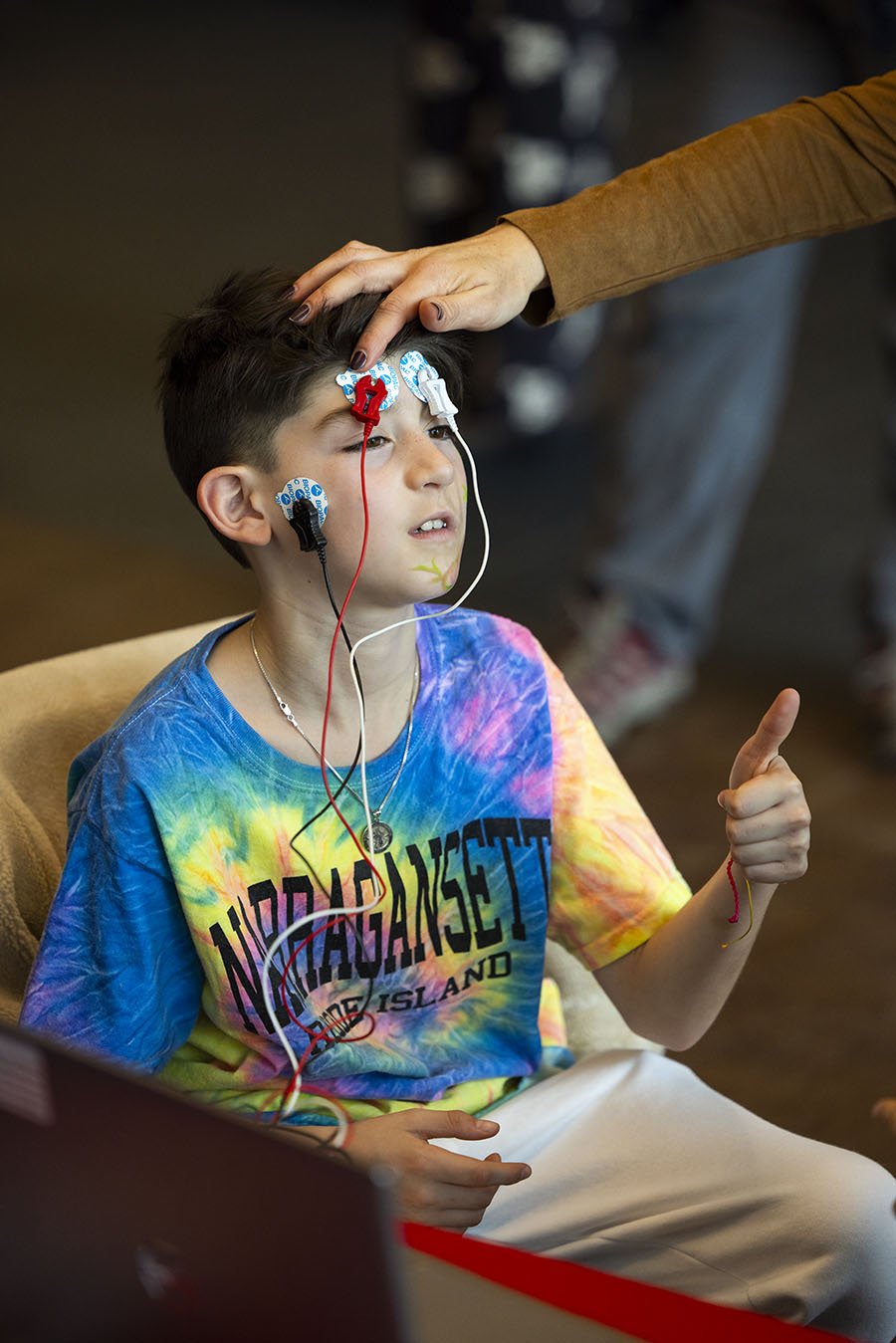 Kids sit in chair with wires connected to their head to see their brain waves in real-time on a monitor.