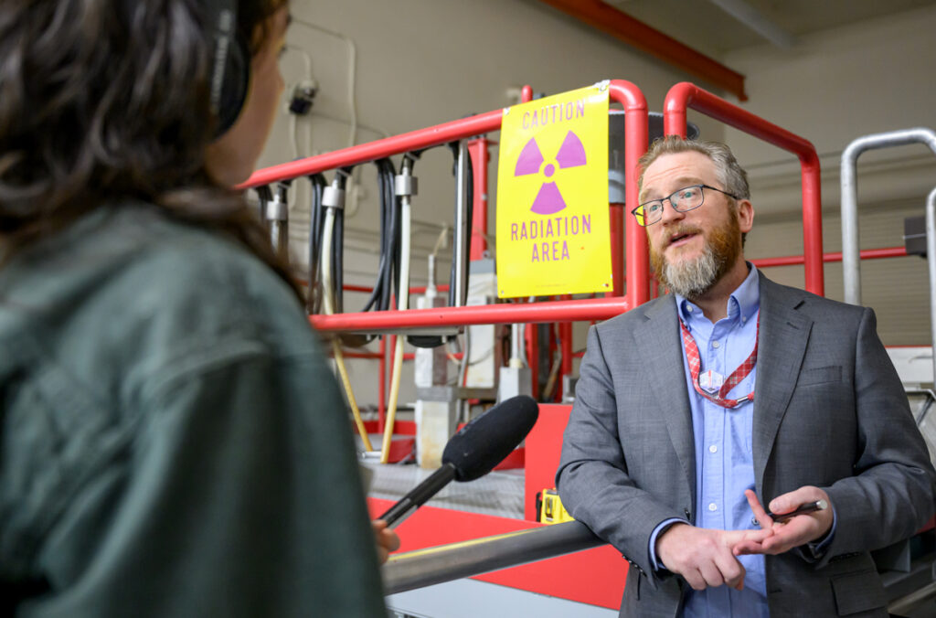 WSU celebrates 65 years of nuclear excellence | WSU Insider Corey Hines speaks to a journalist wearing headphones and holding a microphone during a tour of WSU's Nuclear Science Center.