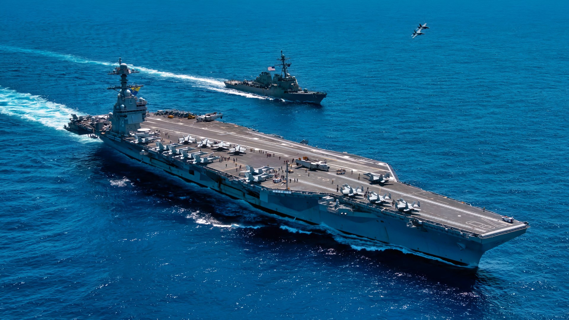 An F/A-18F Super Hornet, attached to the "Blacklions" of Strike Fighter Squadron (VFA) 213 and a F/A-18E Super Hornet, attached to the "Golden Warriors" of Strike Fighter Squadron (VFA) 87 fly over the world's largest aircraft carrier, USS Gerald R. Ford (CVN 78), the Arleigh Burke-class guided-missile destroyer USS Mahan (DDG 72), April 11, 2025. The Gerald R. Ford Carrier Strike Group is underway in the Atlantic Ocean completing integrated naval warfighting training. Composite Training Unit Exercise (COMPTUEX) is the Joint Force’s most complex integrated training event and prepares naval task forces for sustained high-end Joint and combined combat. Integrated naval training provides America’s civilian leaders and commanders highly-capable forces that deter adversaries, underpin American security and economic prosperity, and reassure Allies and partners. (U.S. Navy photo by Mass Communication Specialist 2nd Class Maxwell Orlosky