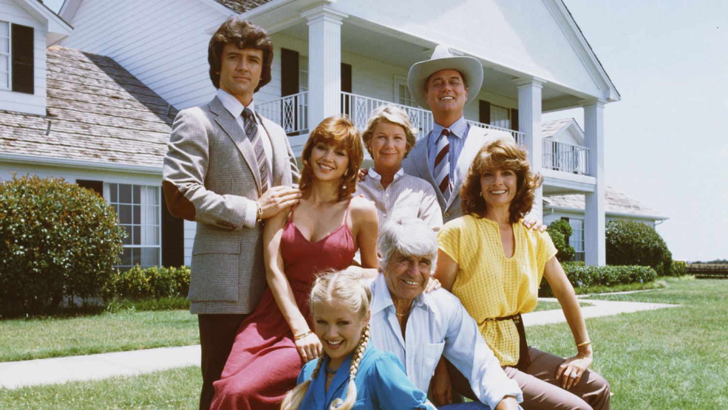 A promotional still from the American television series Dallas shows members of the Ewing family as they pose in front of their television home, the Southfork Ranch, Dallas, Texas, 1979. Back row, from left, Patrick Duffy (as Bobby Ewing) (standing), Victoria Principal (as Pamela Barnes Ewing) (in red dress), Barbara Bel Geddes (as Eleanor Southworth Miss Ellie Ewing), and Larry Hagman (as John Ross J.R. Ewing, Jr.). Front row, from left, Charlene Tilton (as Lucy Ewing), Jim Davis (1909 - 1981) (as John Ross 'Jock' Ewing), and Linda Gray (as Sue Ellen Ewing).