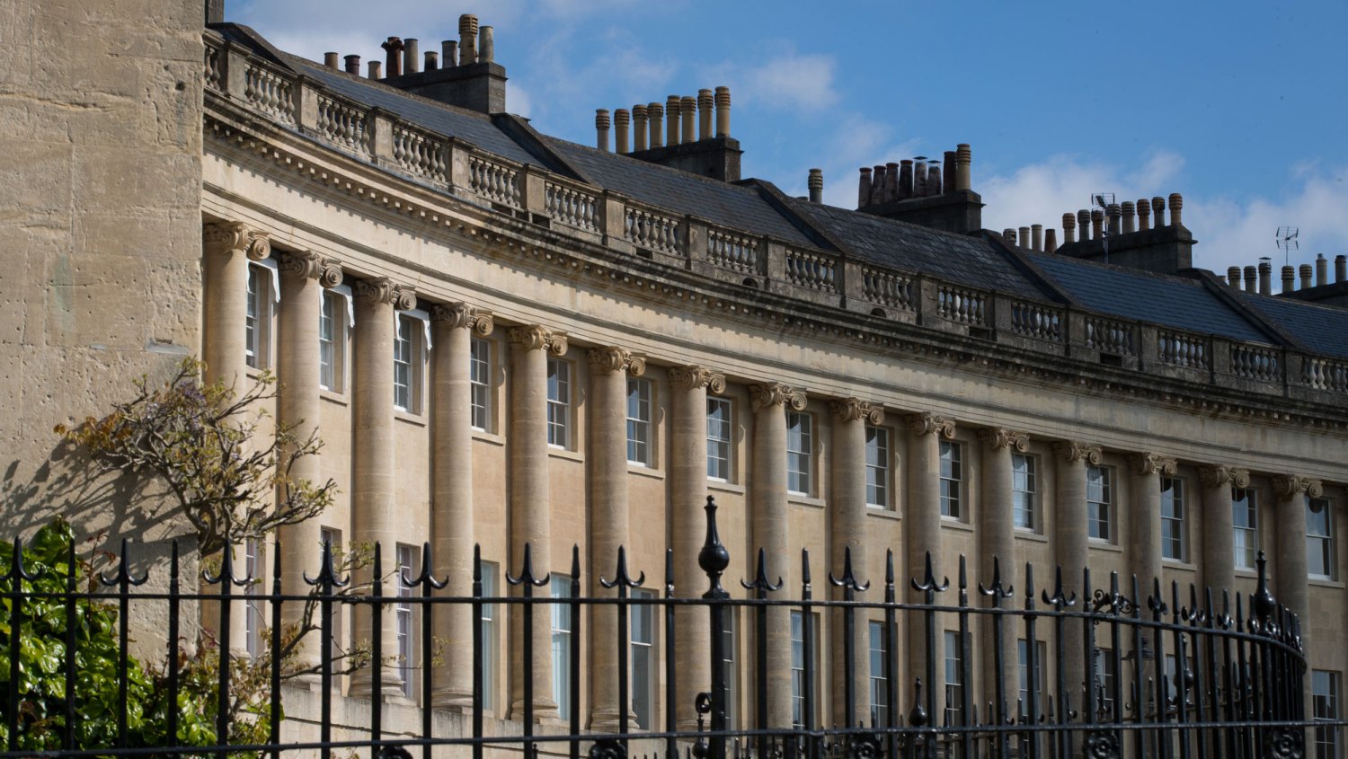 Bridgerton Filming Location_The spring sunshine illuminates part of the facade of the Royal Crescent on April 19, 2017 in Bath, England. Designed by the architect John Wood the Younger and built between 1767 and 1774, the Grade I Listed Royal Crescent is a row of 30 terraced houses laid out in a 500-foot-long (150 m) crescent and is among the greatest examples of Georgian architecture to be found in the UK and was one of the reasons why Bath was awarded UNESCO World Heritage status in 1987. Although some changes have been made to the various interiors of the houses over the years, the Georgian stone exterior facade essentially remains much as it was when it was first built. A series of events are planned to celebrate the 250th anniversary of the laying of the Royal Crescent's first foundation on May 19, 1767.