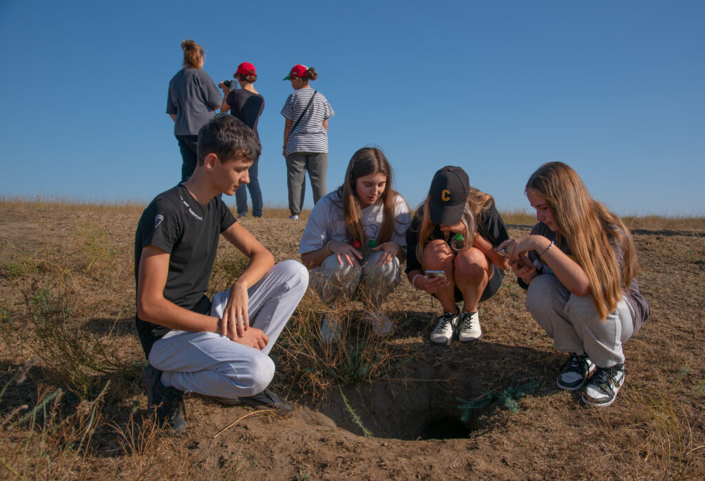 School children at the entrance of a steppe marmot burrow. Tarutino Steppe, Ukraine.