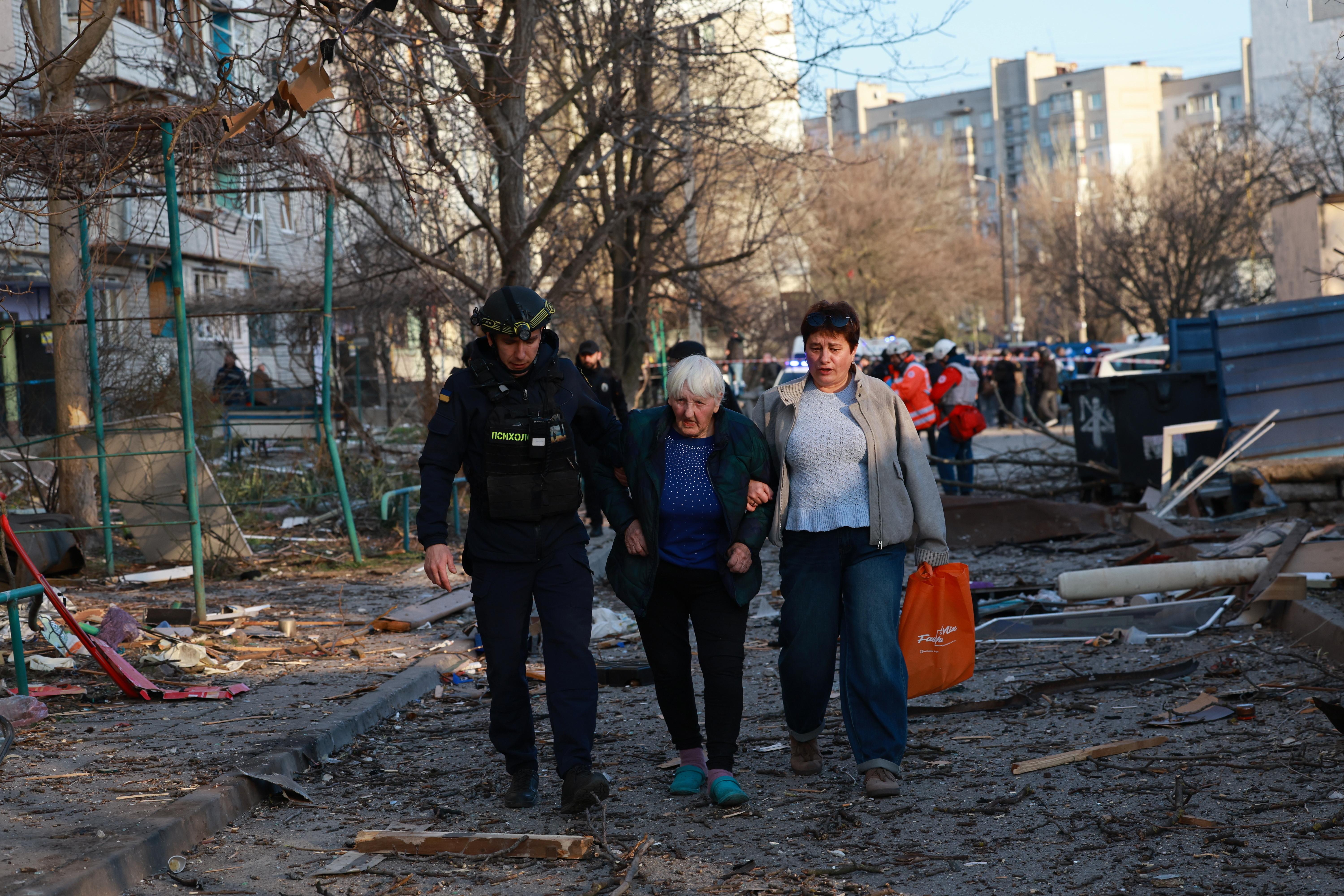 A rescuer helps an elderly woman to leave her home...