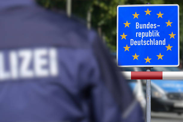 Sign reading “Bundesrepublik Deutschland” with EU stars near a checkpoint, with a police officer in the foreground.